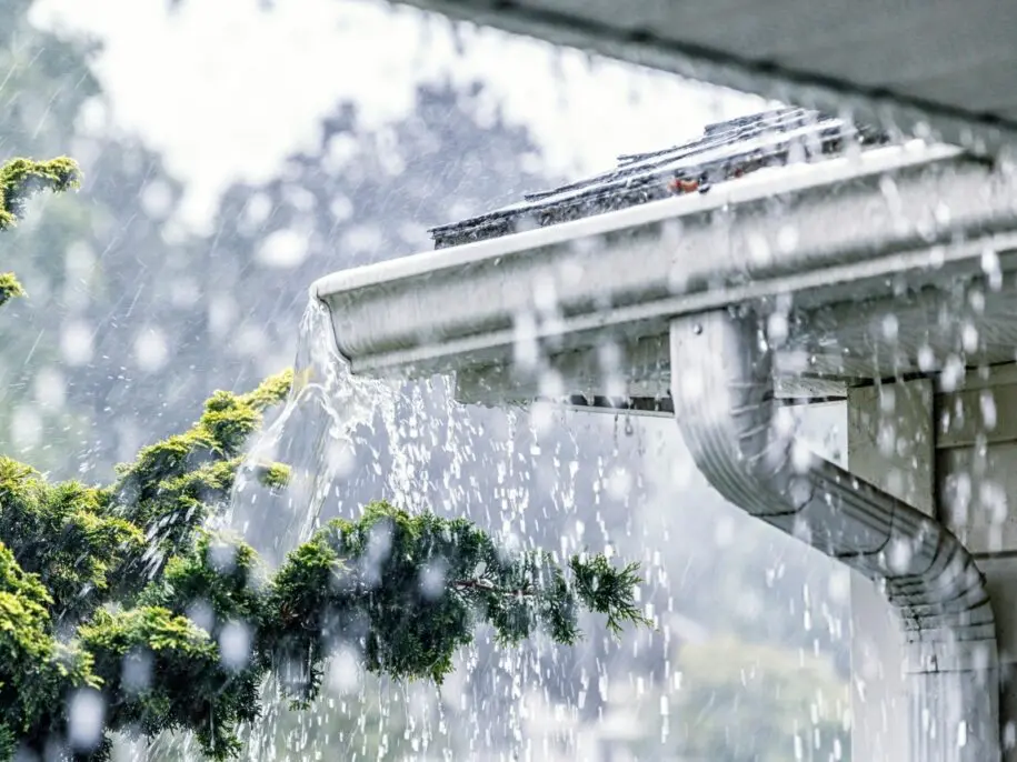 Heavy rainwater spilling from white gutter – clogged gutter overflowing during storm.